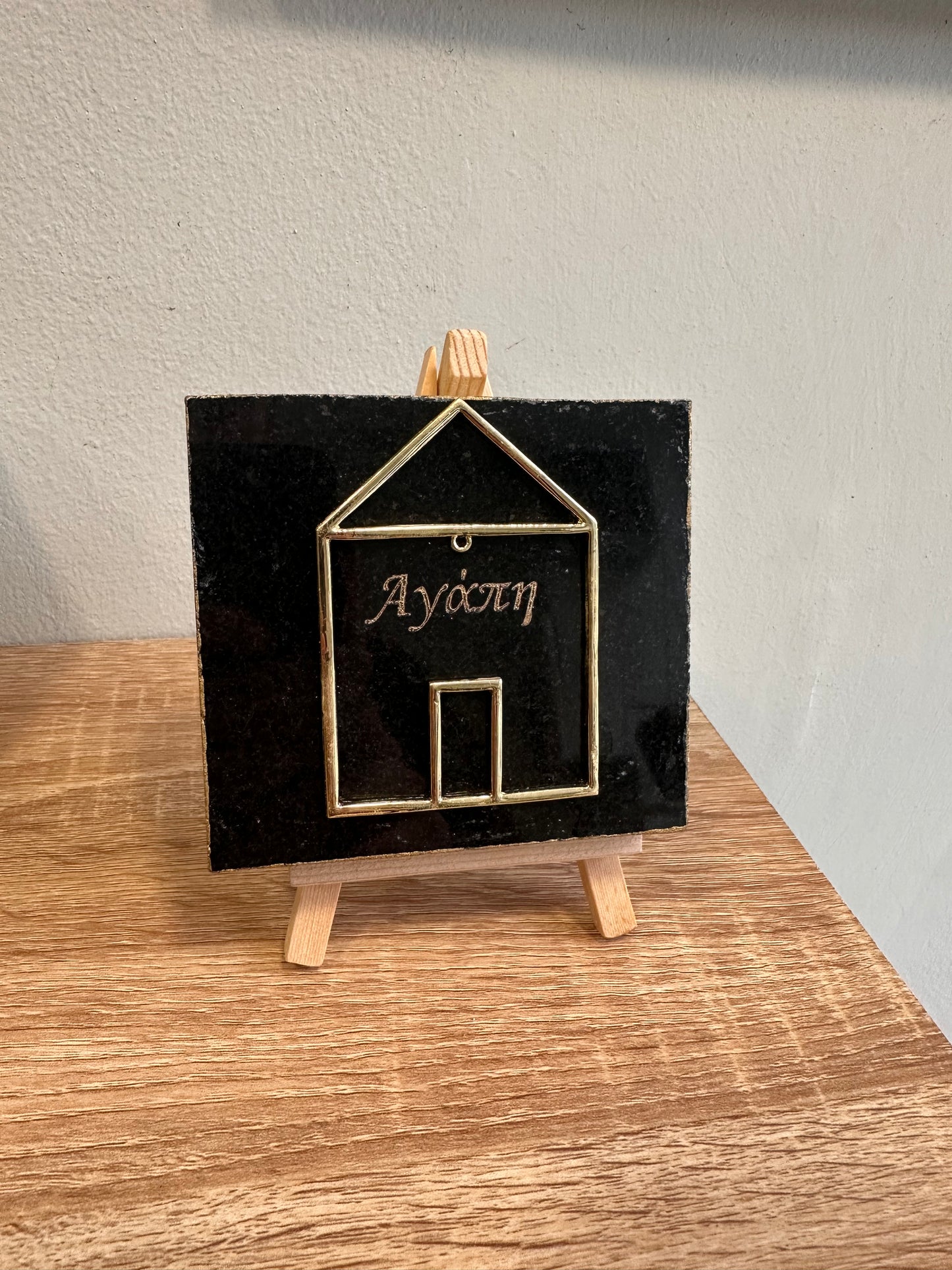 Charm with a metal house engraved on black granite with gold letters and a wooden base